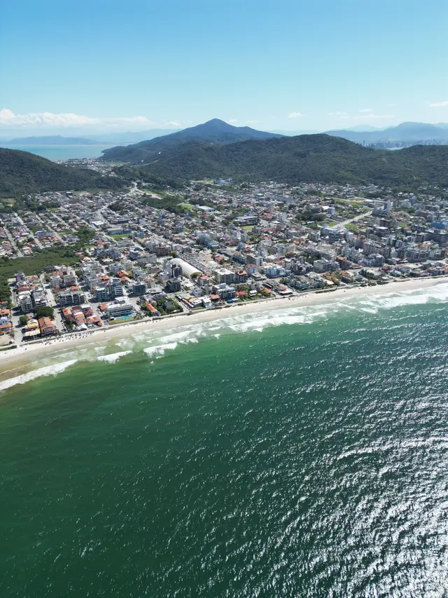 Vista aérea de Bombas com a cidade espalhada até o pé dos morros e um pico em destaque ao fundo.